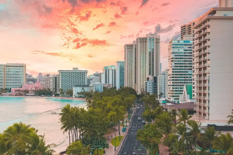 Waikīkī shoreline, palm trees, city buildings, and Kalākaua Avenue at sunset