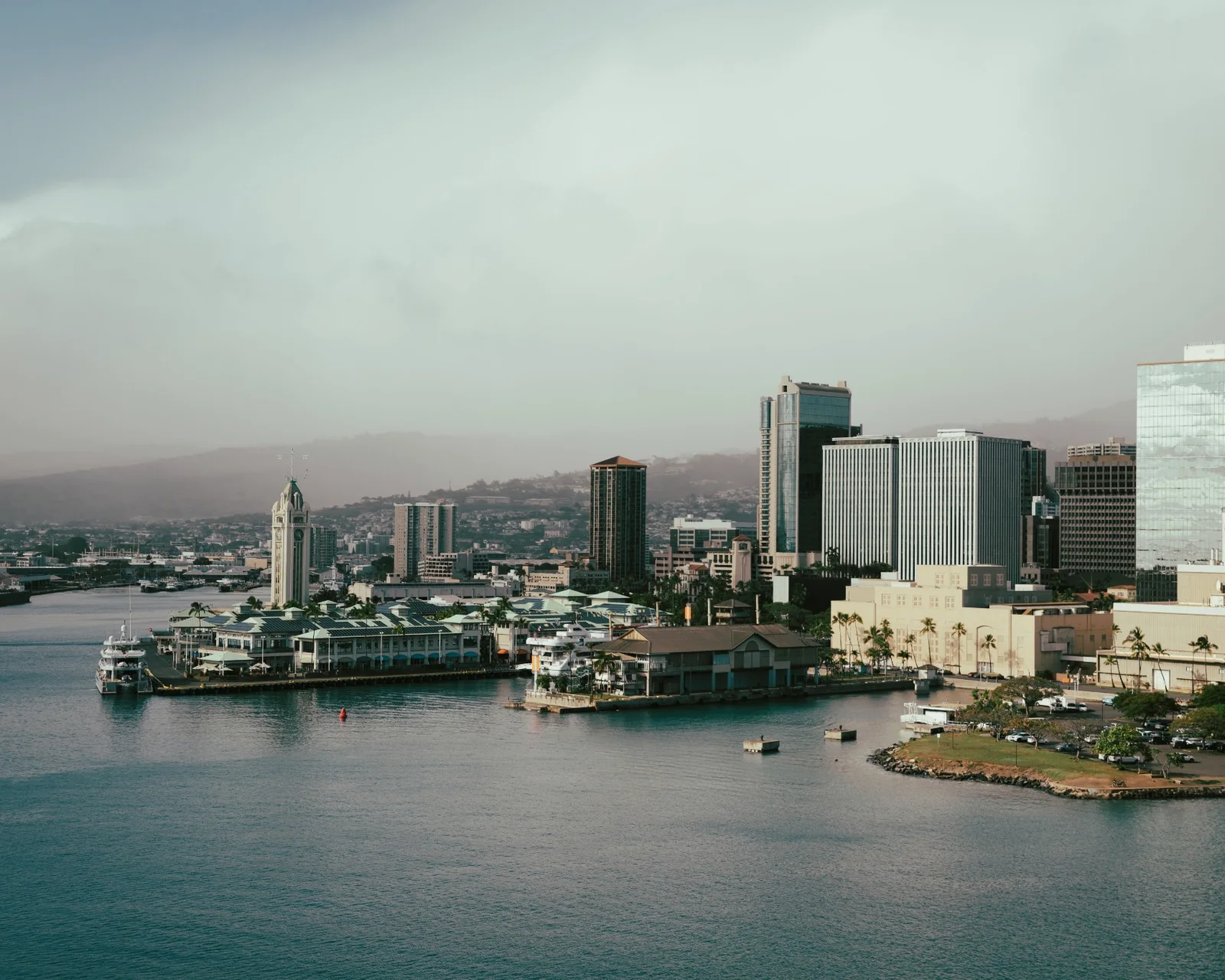 Aerial view of Honolulu Harbor, waterfront buildings, and the Oʻahu city skyline beneath low clouds