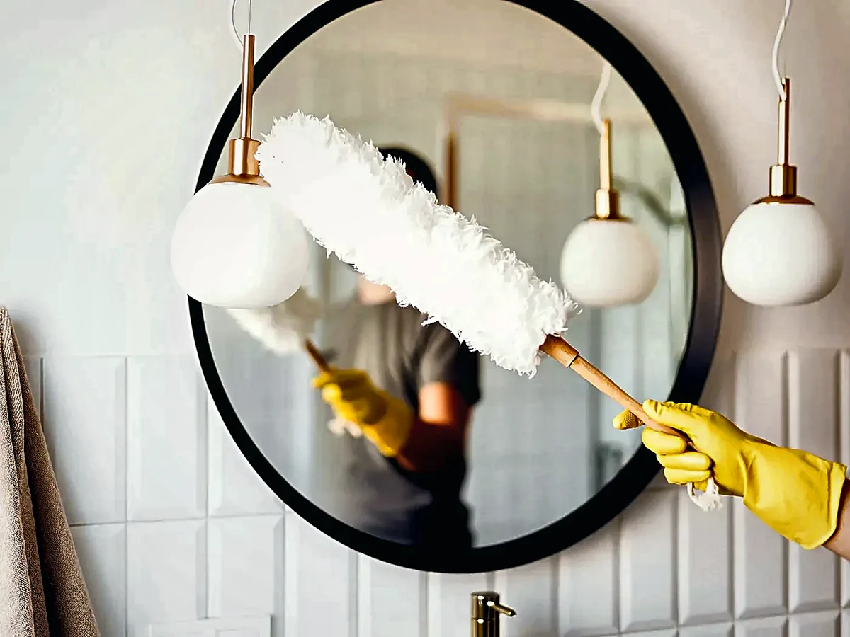 Cleaning professional dusting a bathroom mirror and pendant lights