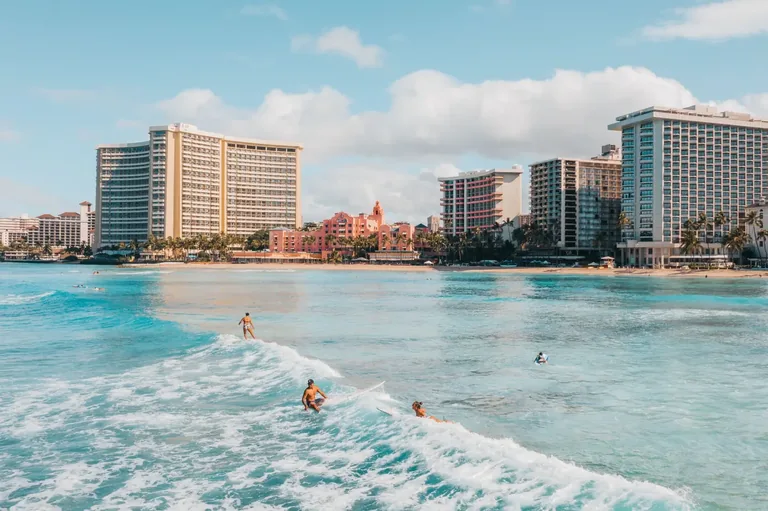Surfers in the ocean with Waikīkī beachfront buildings behind them